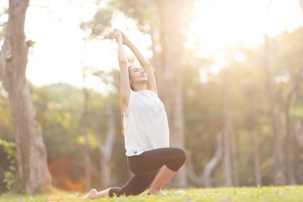 woman stopped after exercising at the garden, sitting on a exercise mat, inhaling deeply by closing her eyes.