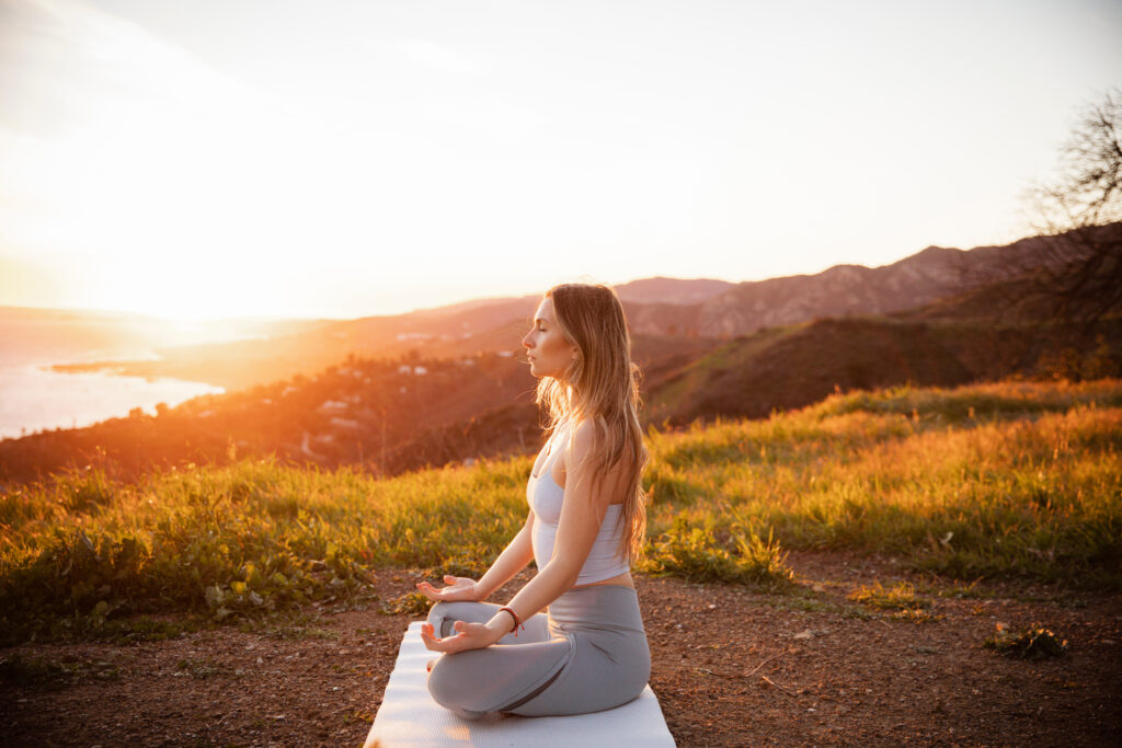 Side view of sportswoman meditating while sitting on exercise mat against mountains during sunset