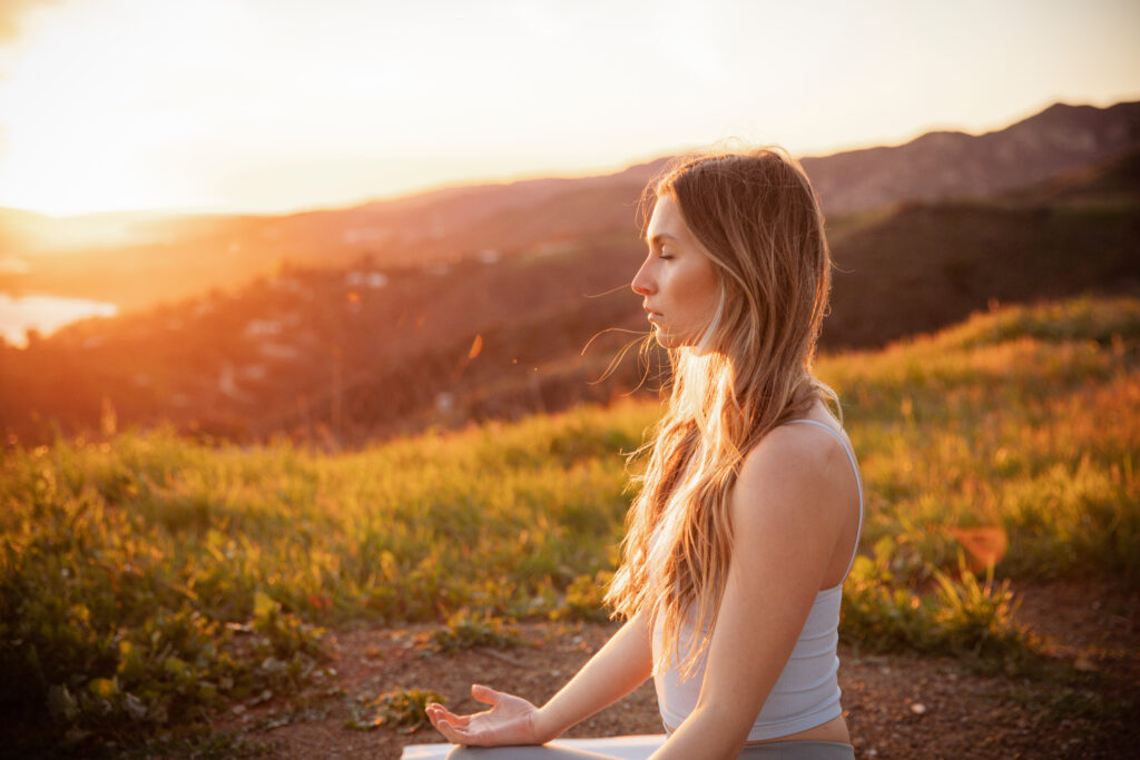 woman with eyes closed practicing breathwork on mountain during