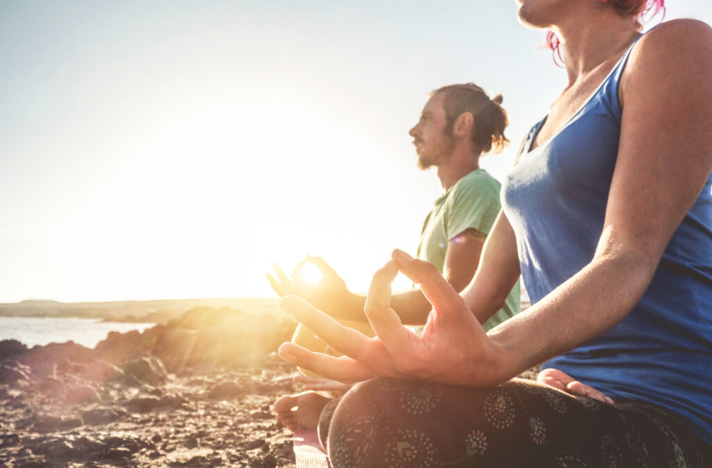 Couple doing yoga outdoor at sunrise in nature - Woman and man meditating together at morning time - Concept of fitness exercise for healthy lifestyle and positive mind - Focus on woman left hand