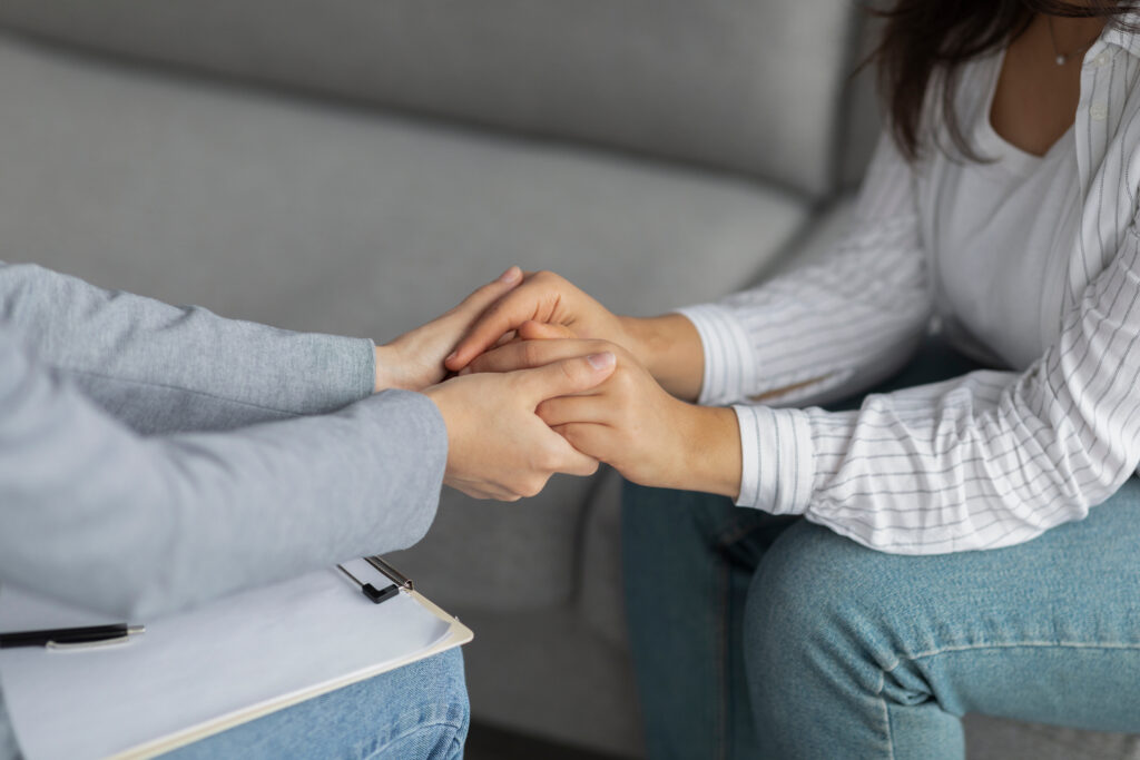 Professional compassion. Psychotherapist supporting depressed woman, holding her hands, sitting in clinic. Psychologist comforting young female patient with mental disorder