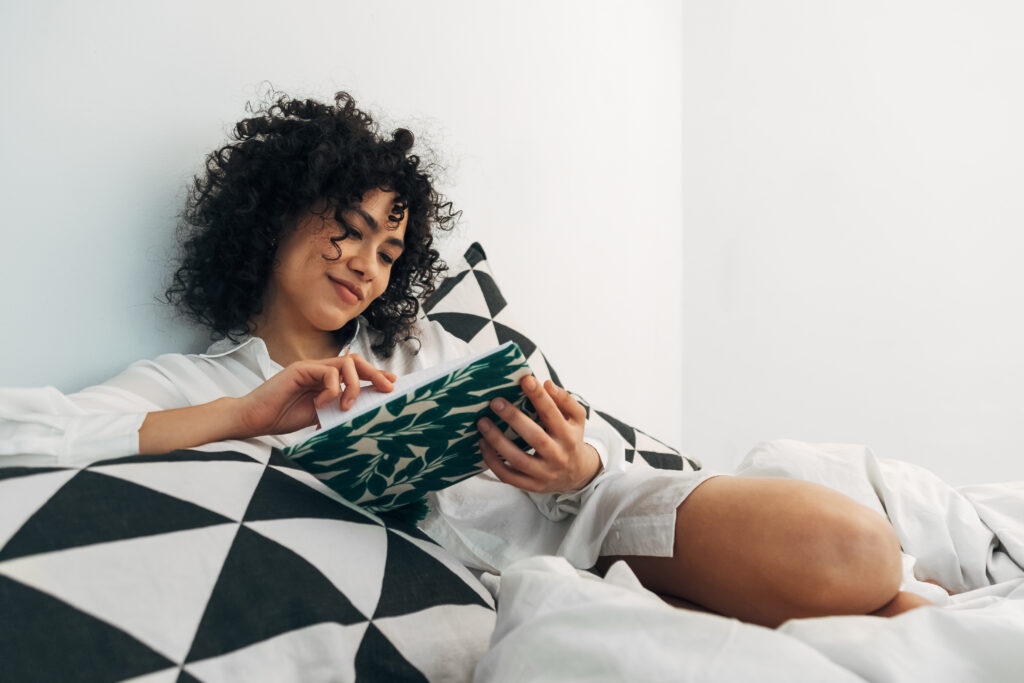 Happy young woman relaxes reading journal notes on bed. Copy space.Lifestyle concept.