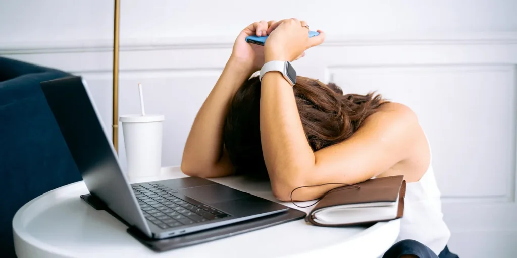 woman with head on table next to laptop