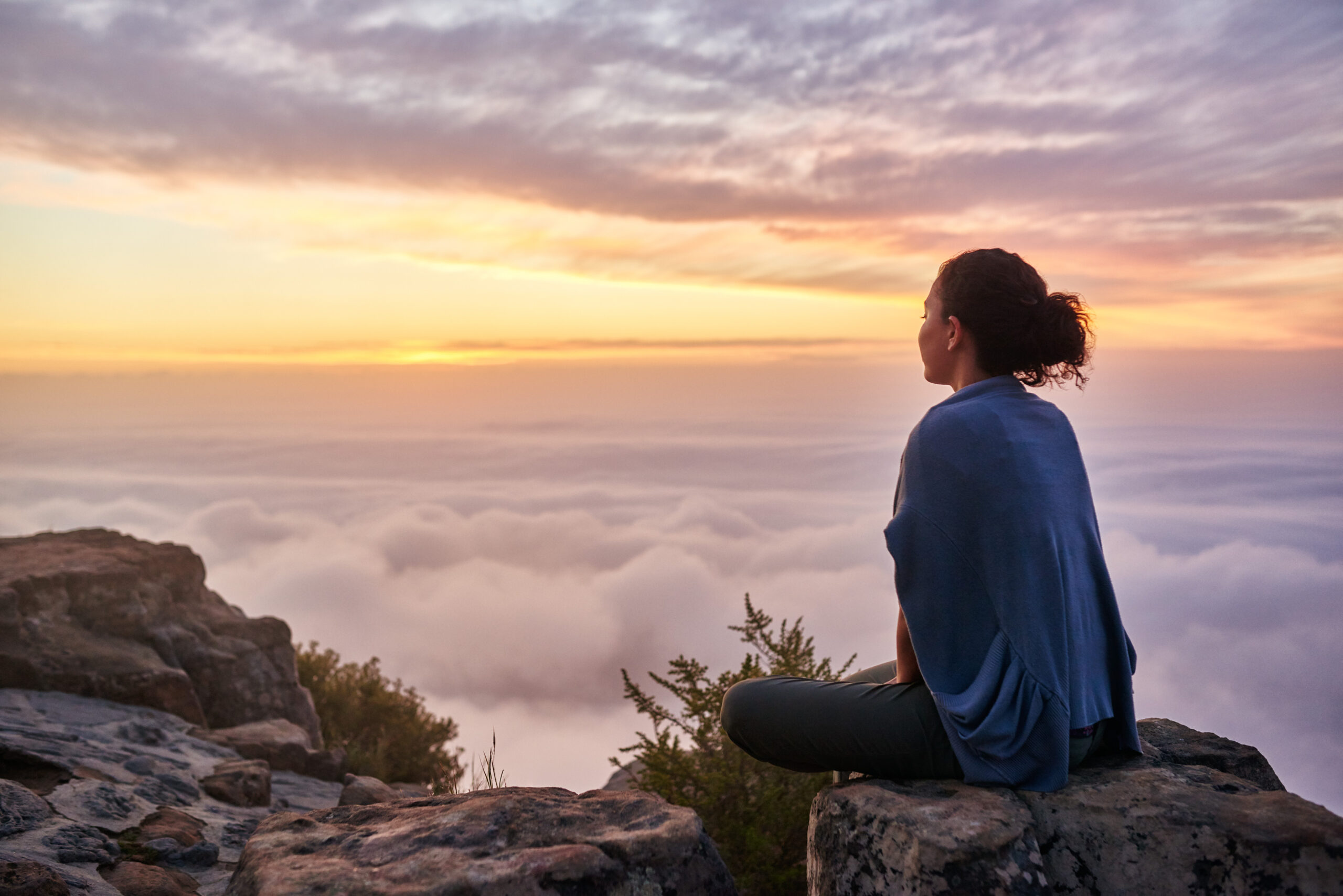 A woman sitting on a rock at sunset, looking out over the water