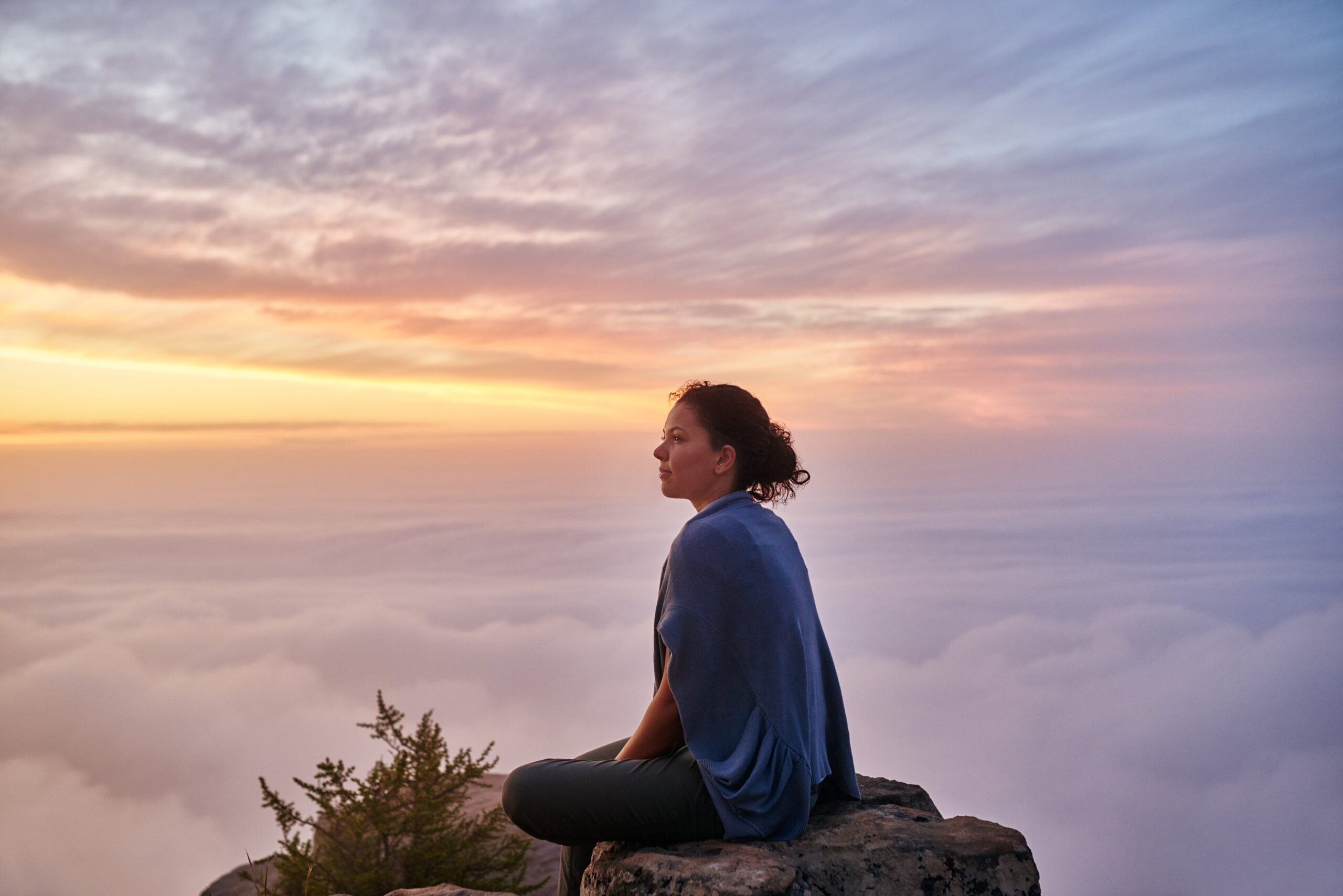 A woman sitting on a rock at sunset, looking out over the water