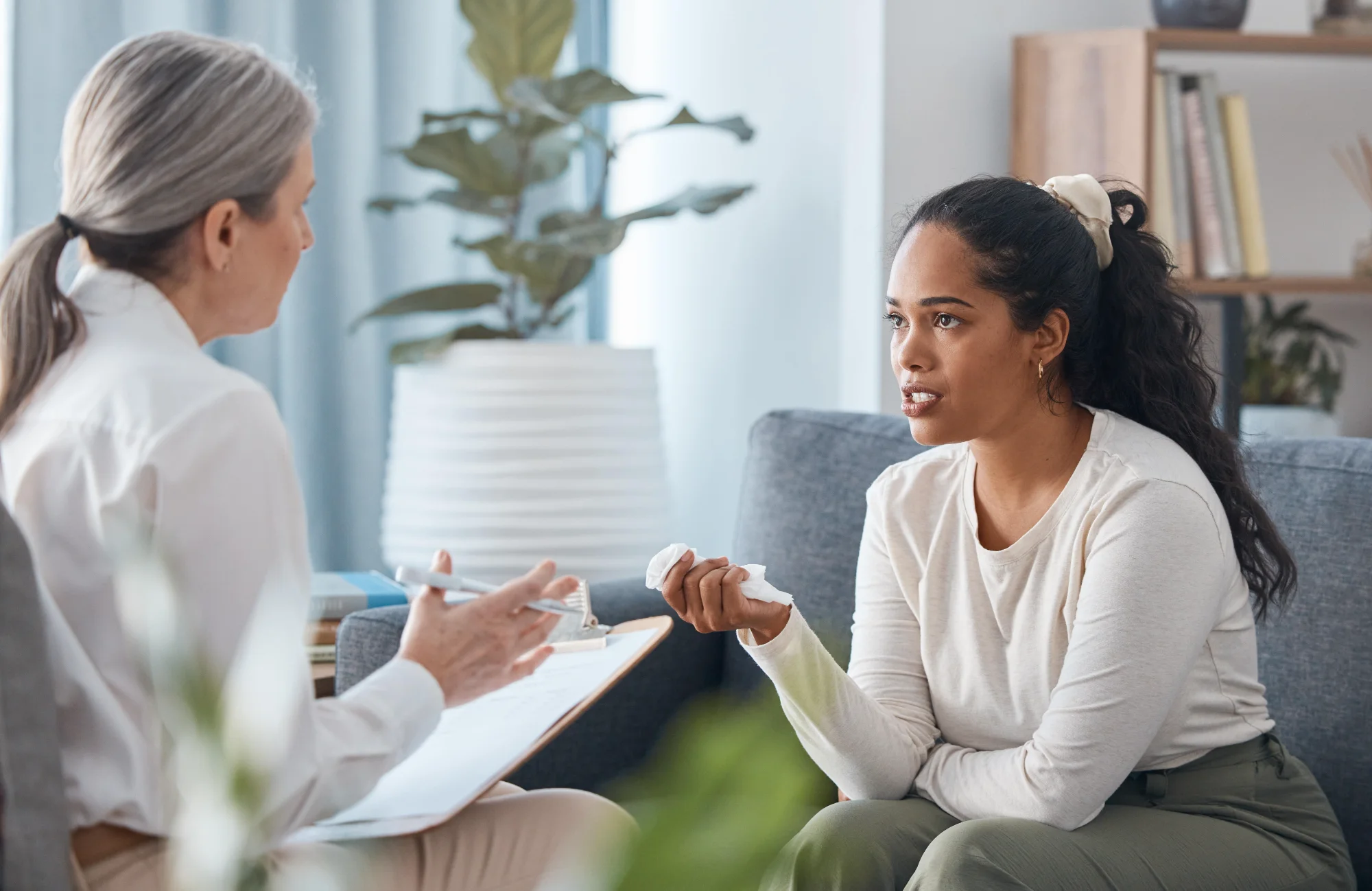 A therapist taking notes while a young woman talks during a one-on-one session