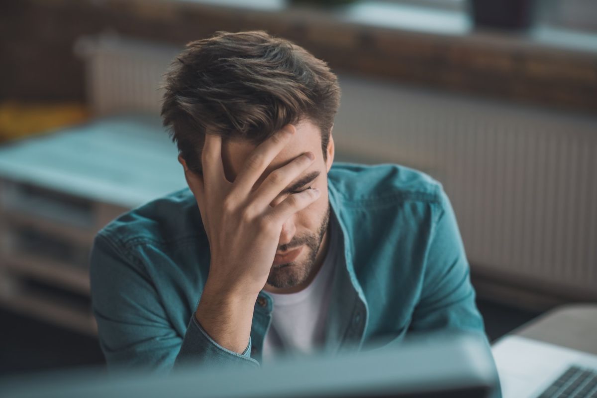 A man with his hand to his forehead, feeling the weight of stress